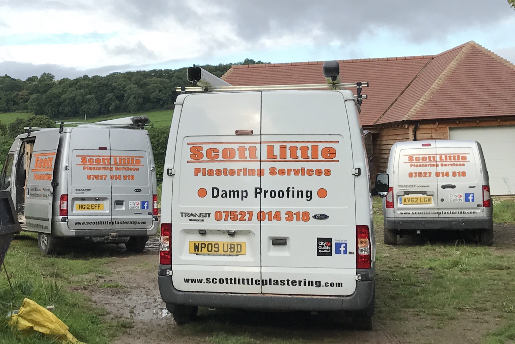 Three Scott Little Plastering Services vans with orange livery parked outside a barn