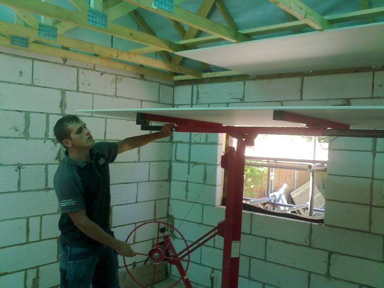 Lifting a ceiling board into place on a board lifter